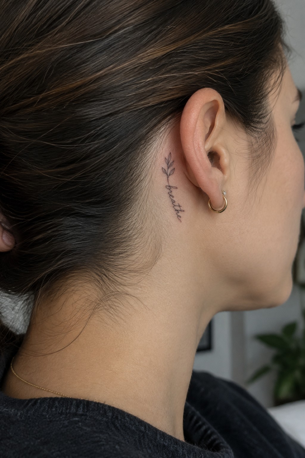 Small fine-line leafy sprig and the word “breathe” tattooed behind a woman’s ear.