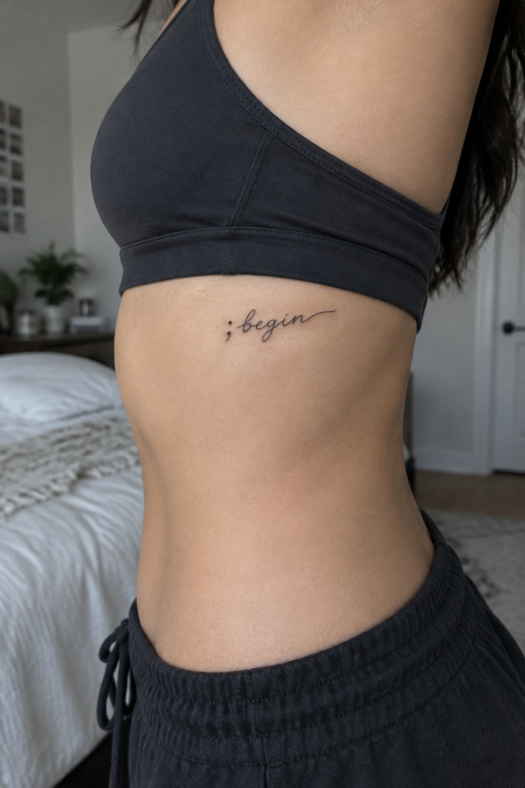 Small fine-line script tattoo reading “begin” on a woman’s side below the bra line.