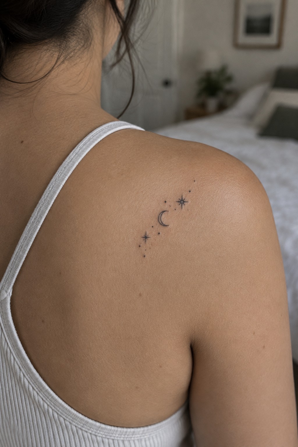 Small fine-line crescent moon, stars, and dots tattoo on the upper shoulder.