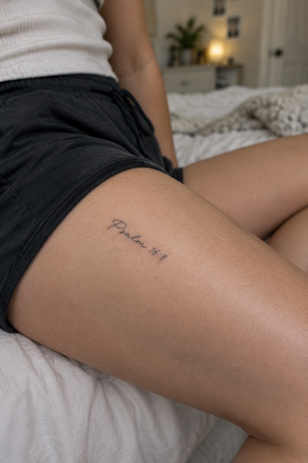 Close up of a small fine line tattoo reading Psalm 16:8 in delicate cursive on the upper thigh.