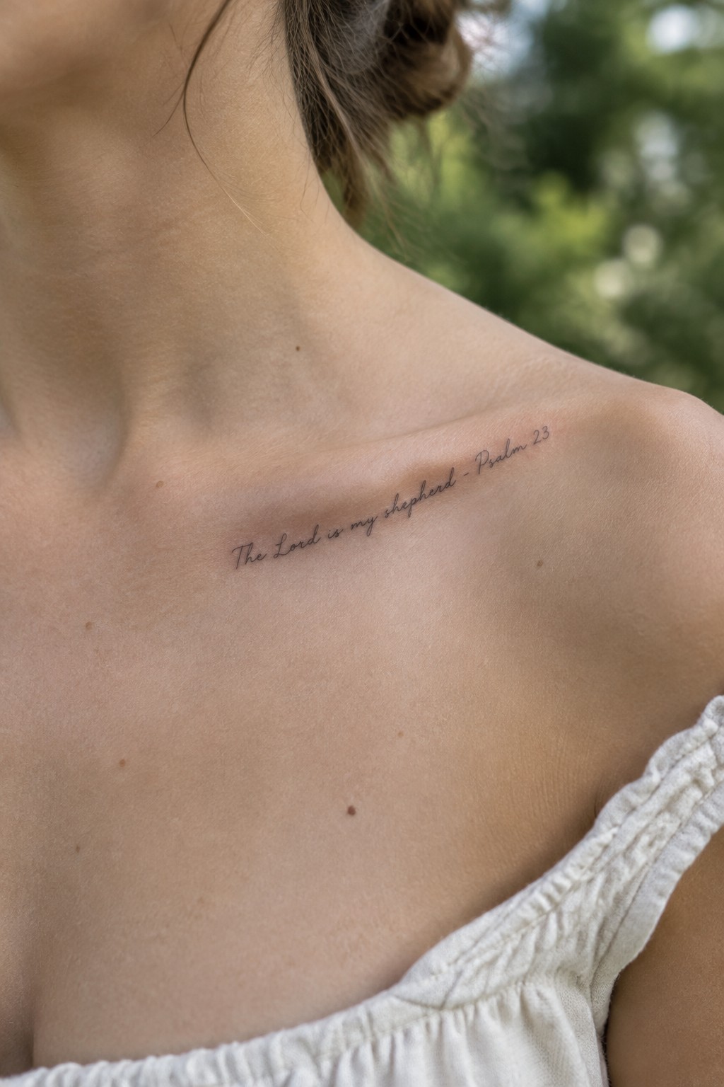 Close-up of collarbone with Psalm 23 tattoo on light skin above white ruffled top.
