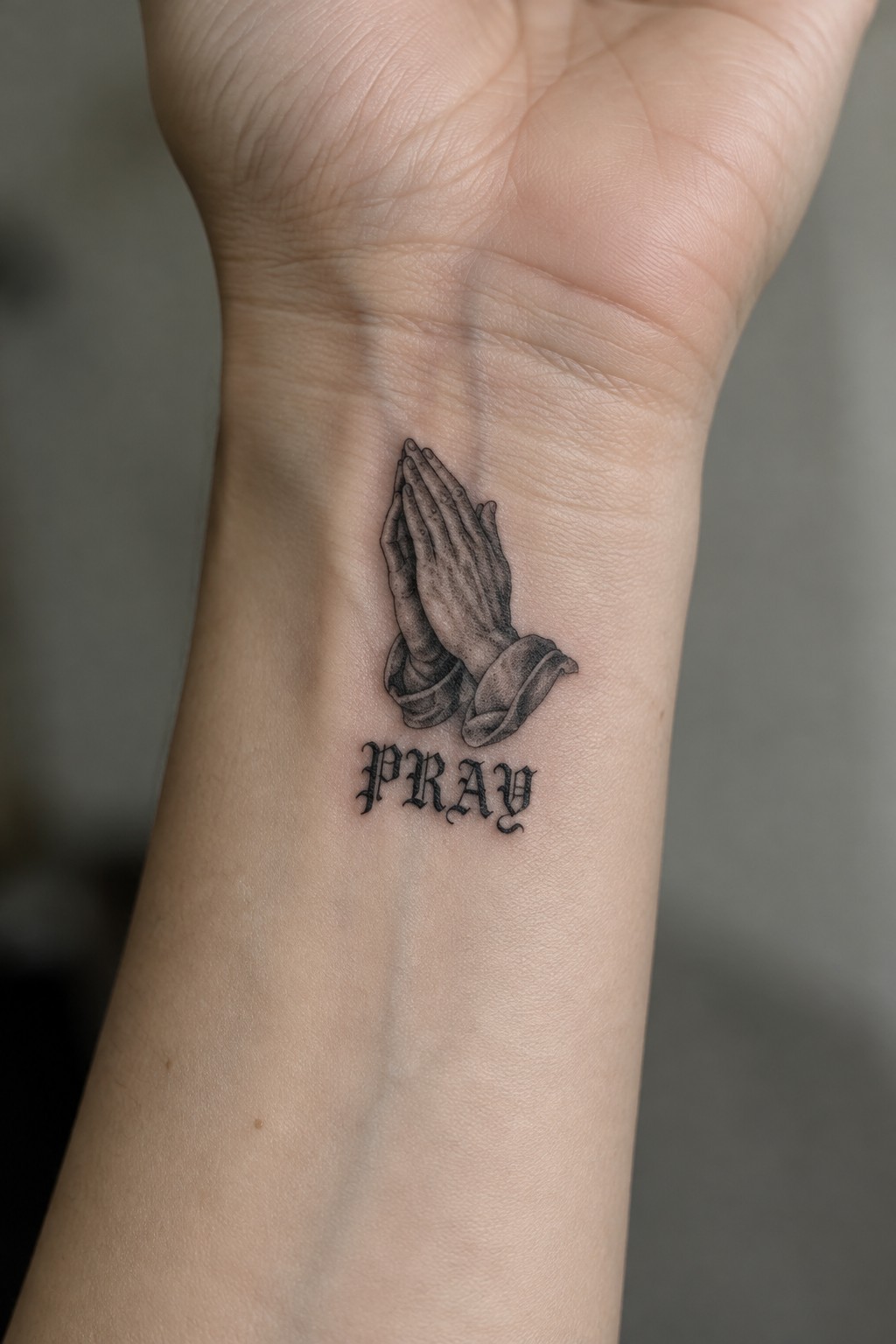 Shaded black-and-gray tattoo of praying hands with 