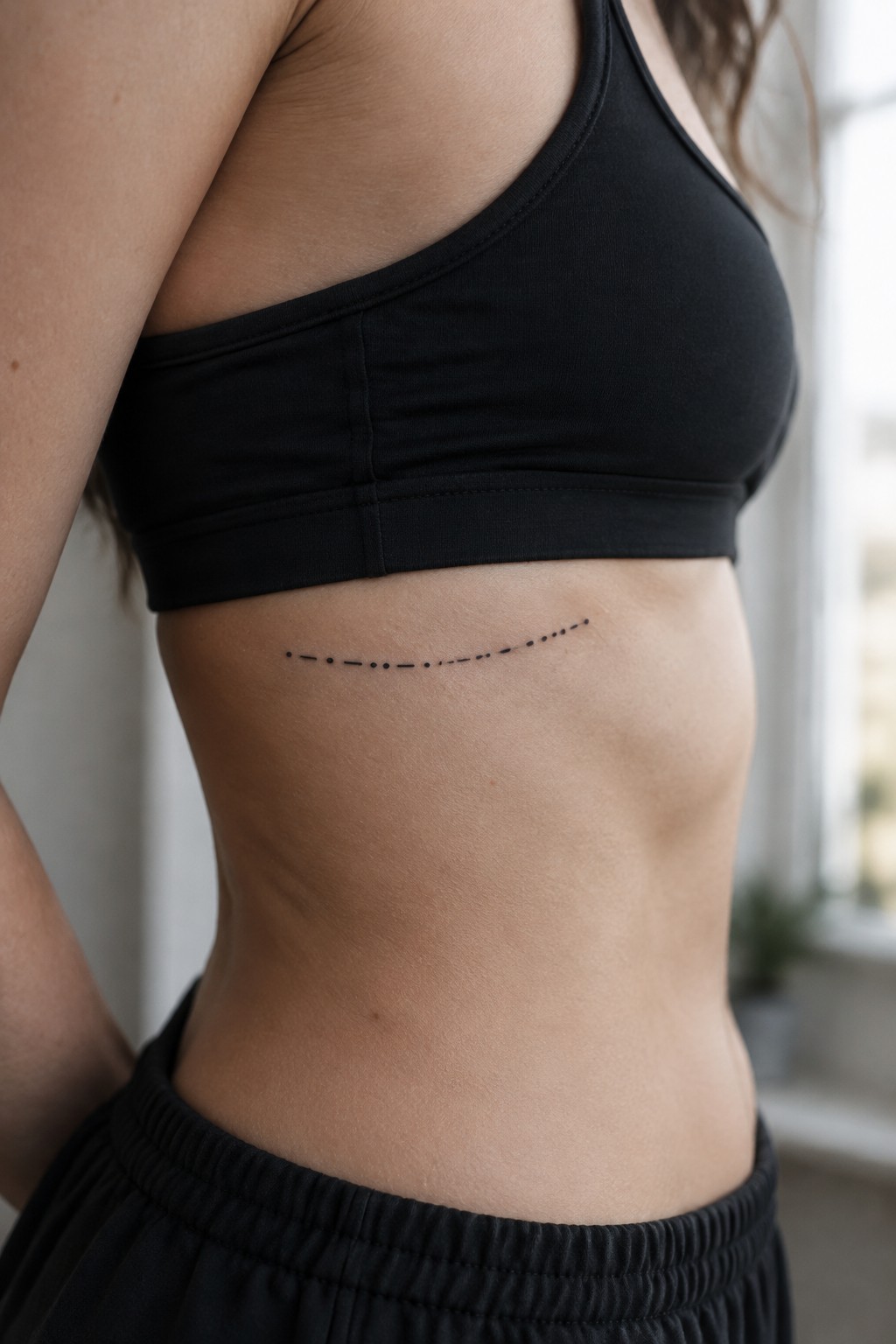 Woman's torso in black sports bra with curved dotted tattoo on side