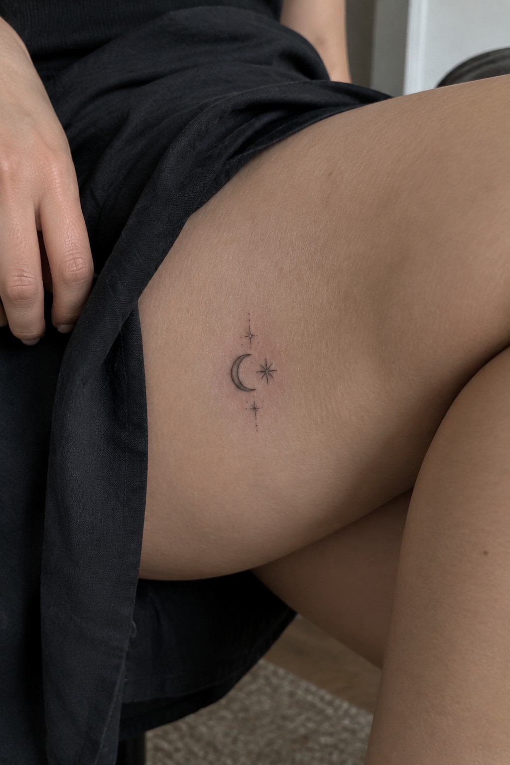 Crescent moon and stars tattoo on thigh beside black fabric and hand
