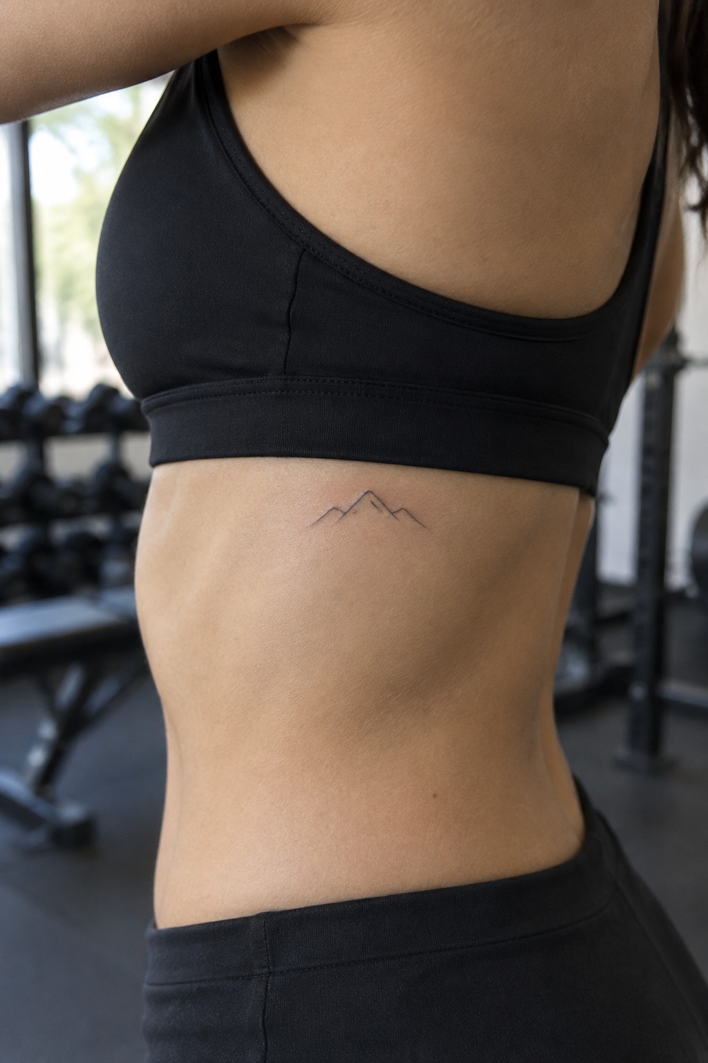 Woman's torso with small mountain tattoo in black sports bra at gym