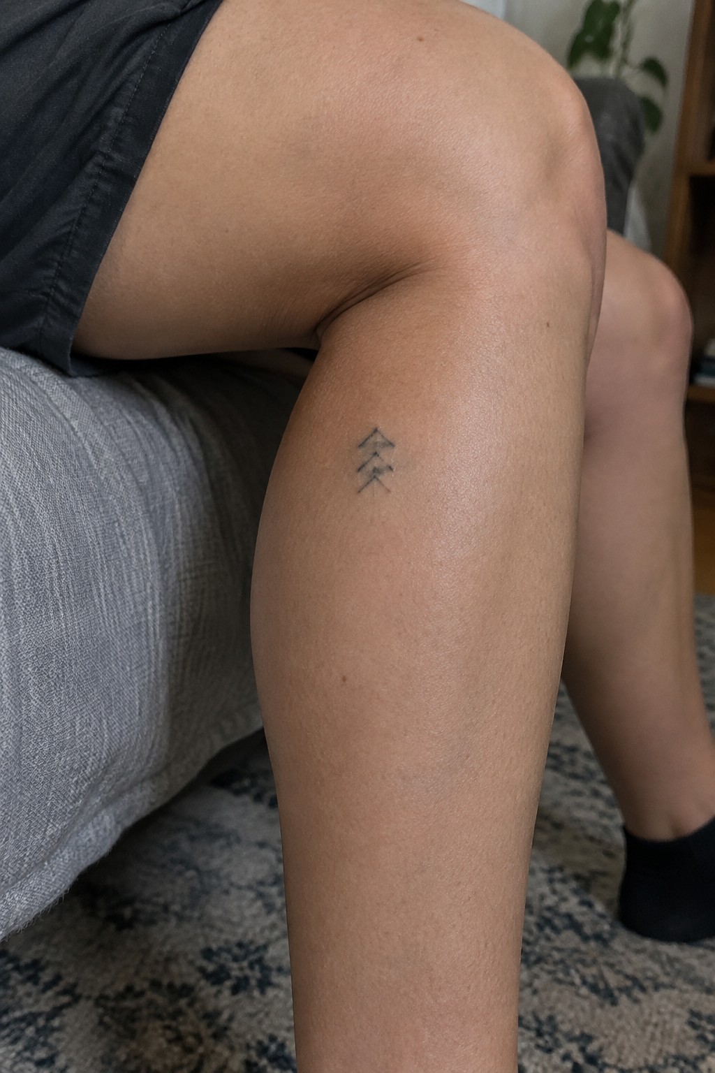 Small black three-arrow tattoo on a bare thigh under dark shorts