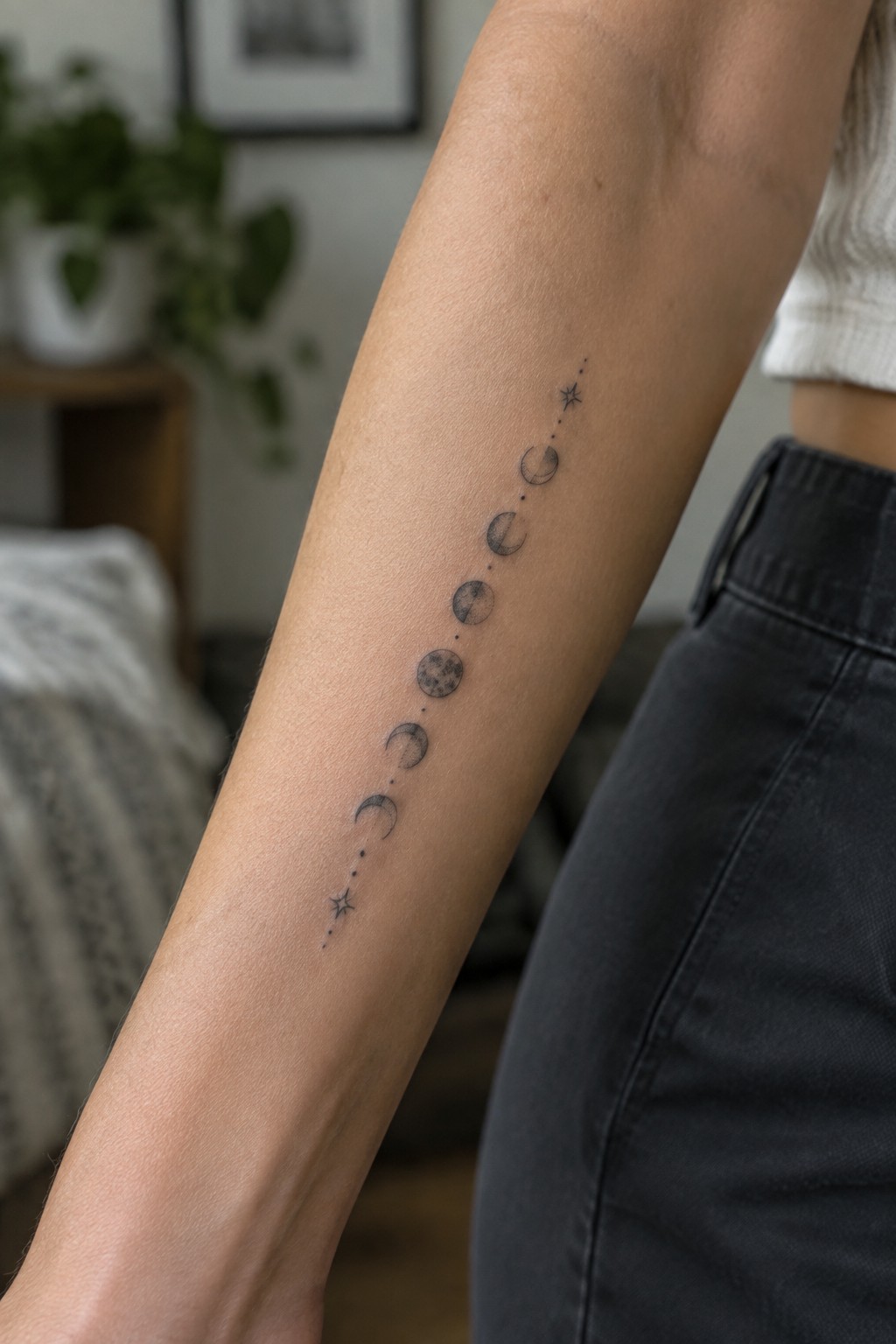 Fine-line moon phase tattoo with small stars and dots arranged vertically along a woman’s forearm.