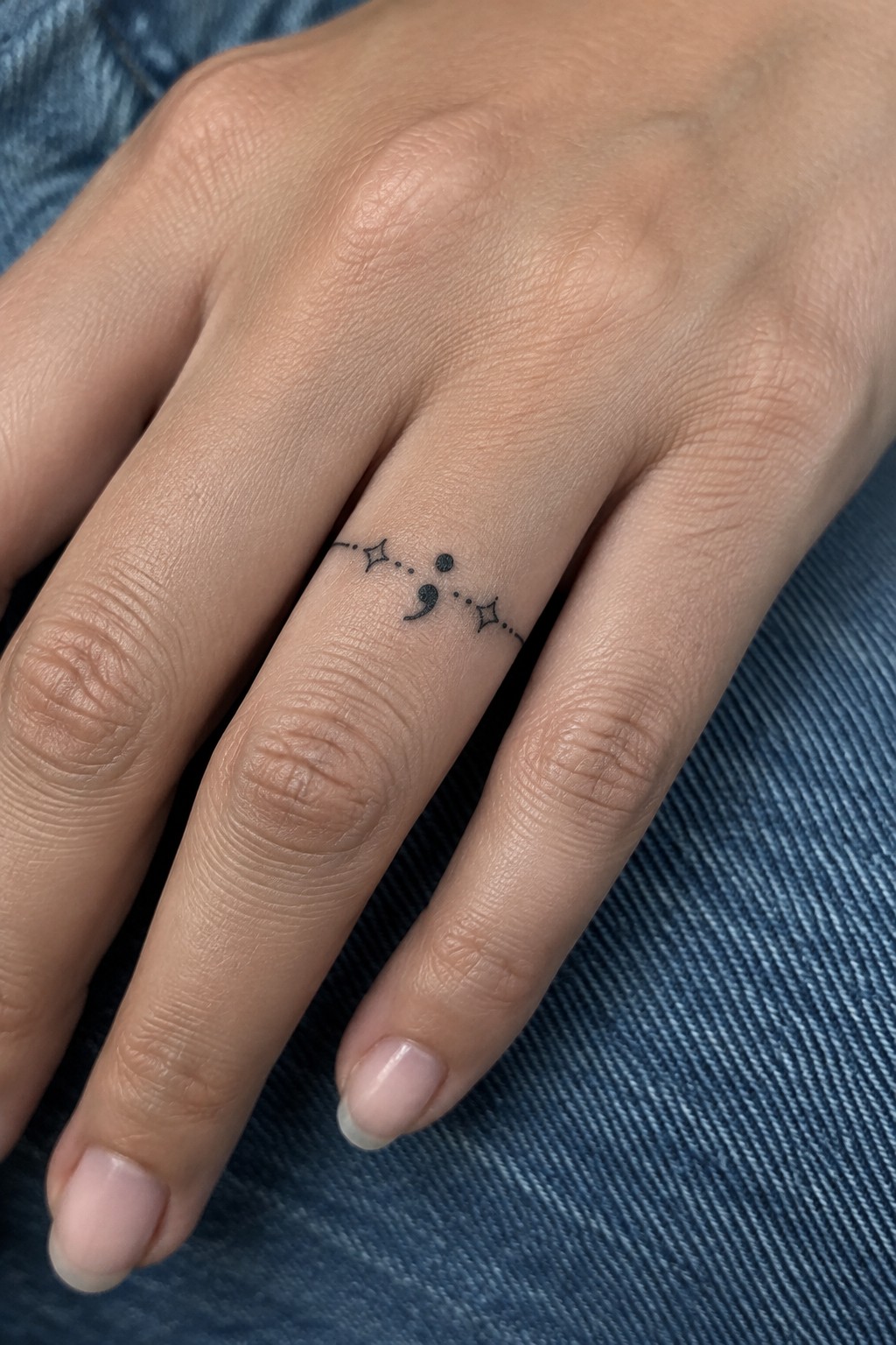 Small black semicolon tattoo with tiny stars and dots on a finger.