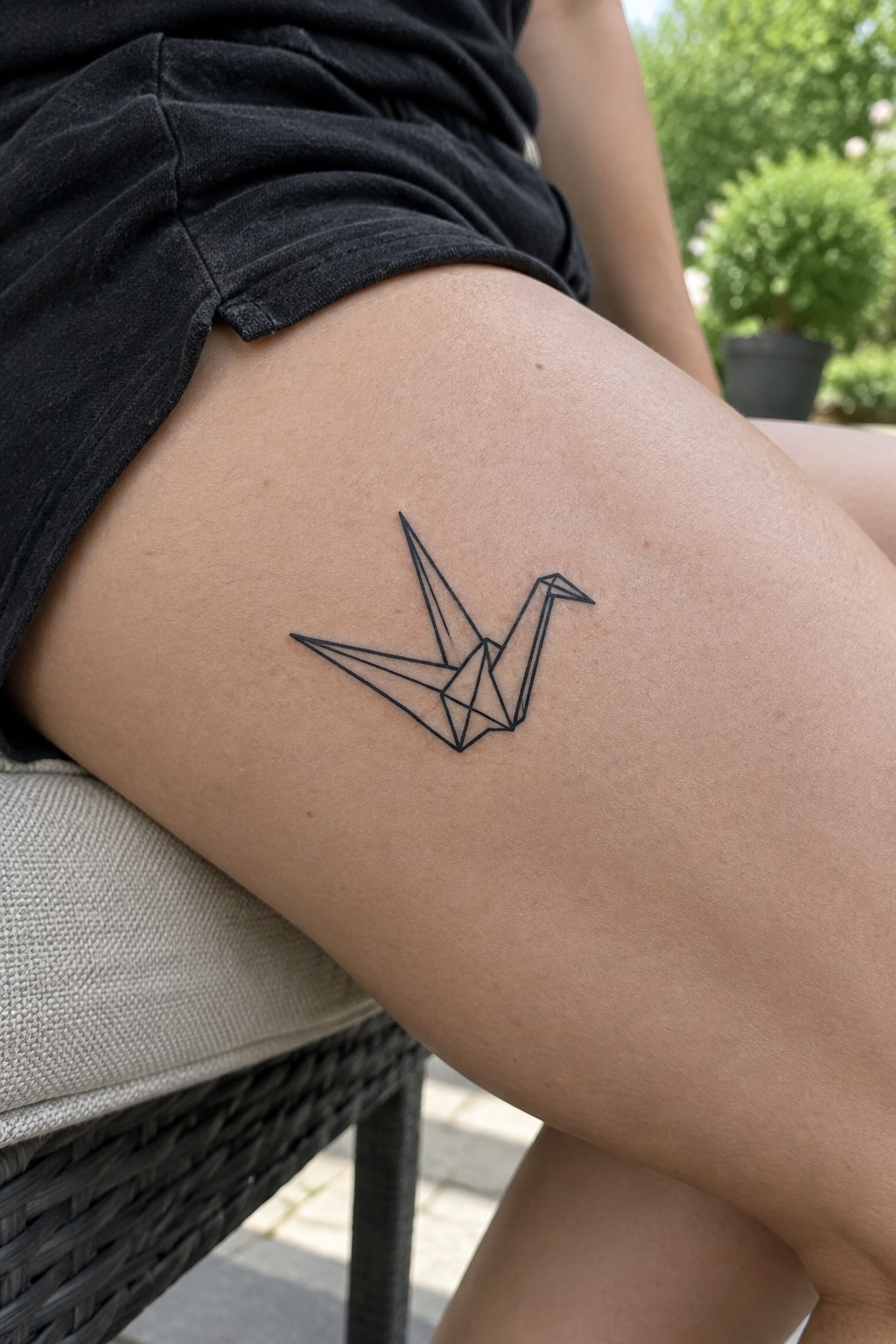 Minimalist black line art origami crane tattoo on the upper thigh