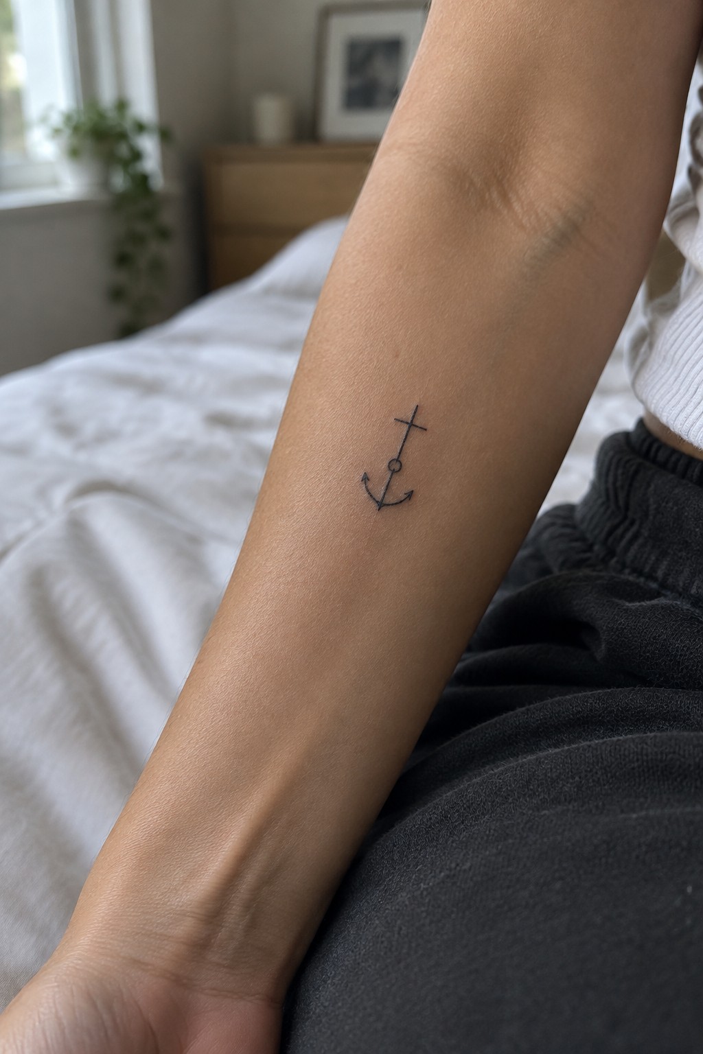 Small black anchor tattoo on forearm of person in white shirt and dark pants