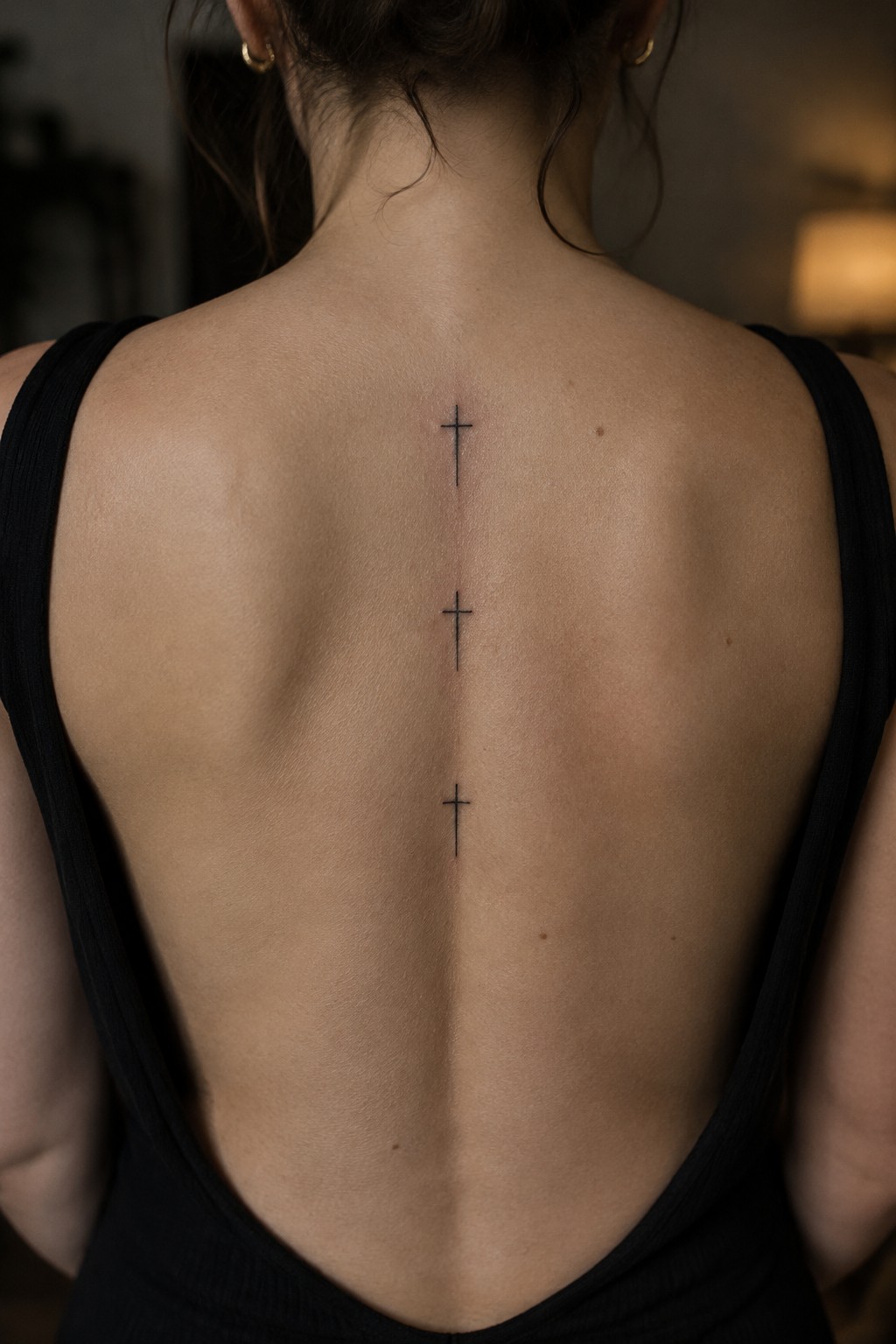 Three small black cross tattoos aligned vertically along a woman's spine on her upper and mid back.
