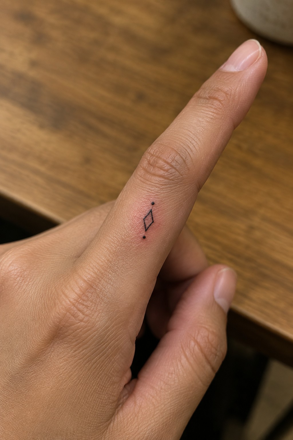 Close-up of finger with small black diamond tattoo and dots on wood