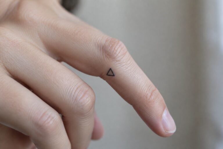 Close up of a tiny black outline triangle tattoo on the side of a finger.