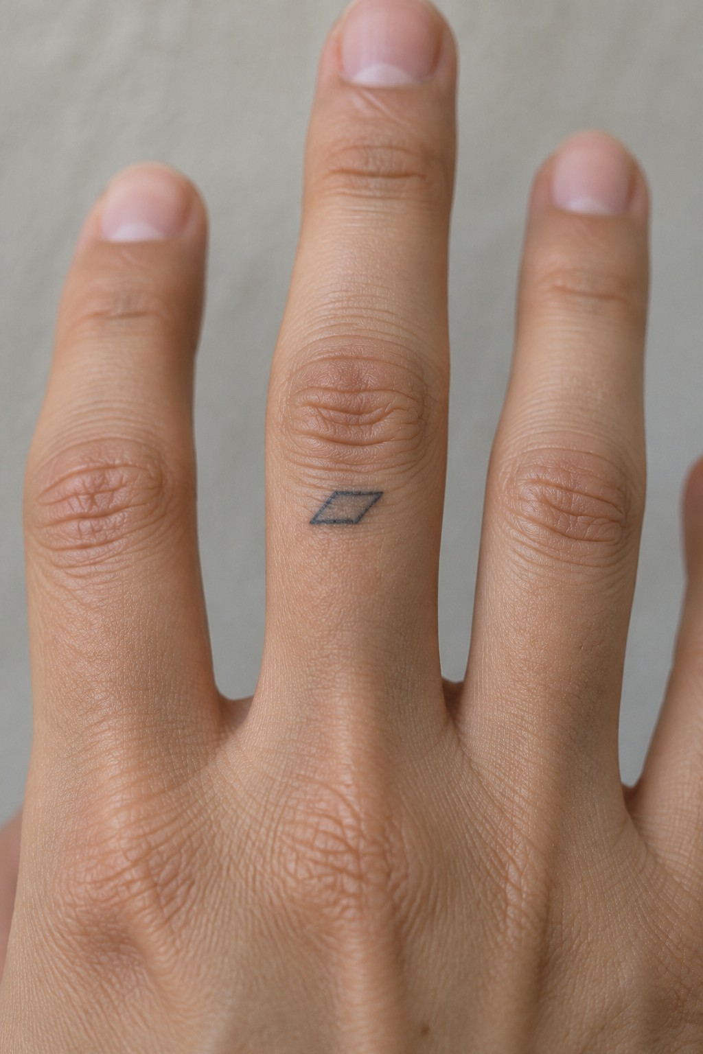 Close-up of a hand with a small black diamond tattoo on the middle finger.