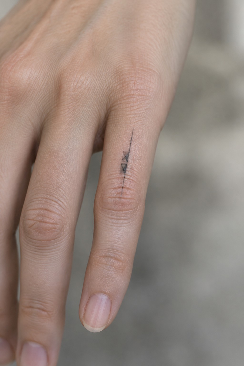 Close-up of hand with minimalist black line tattoo and two small triangles on finger.