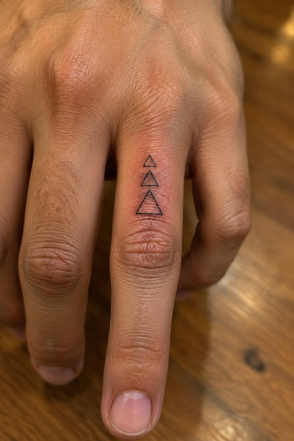 Three black outlined triangles tattooed vertically on a middle finger