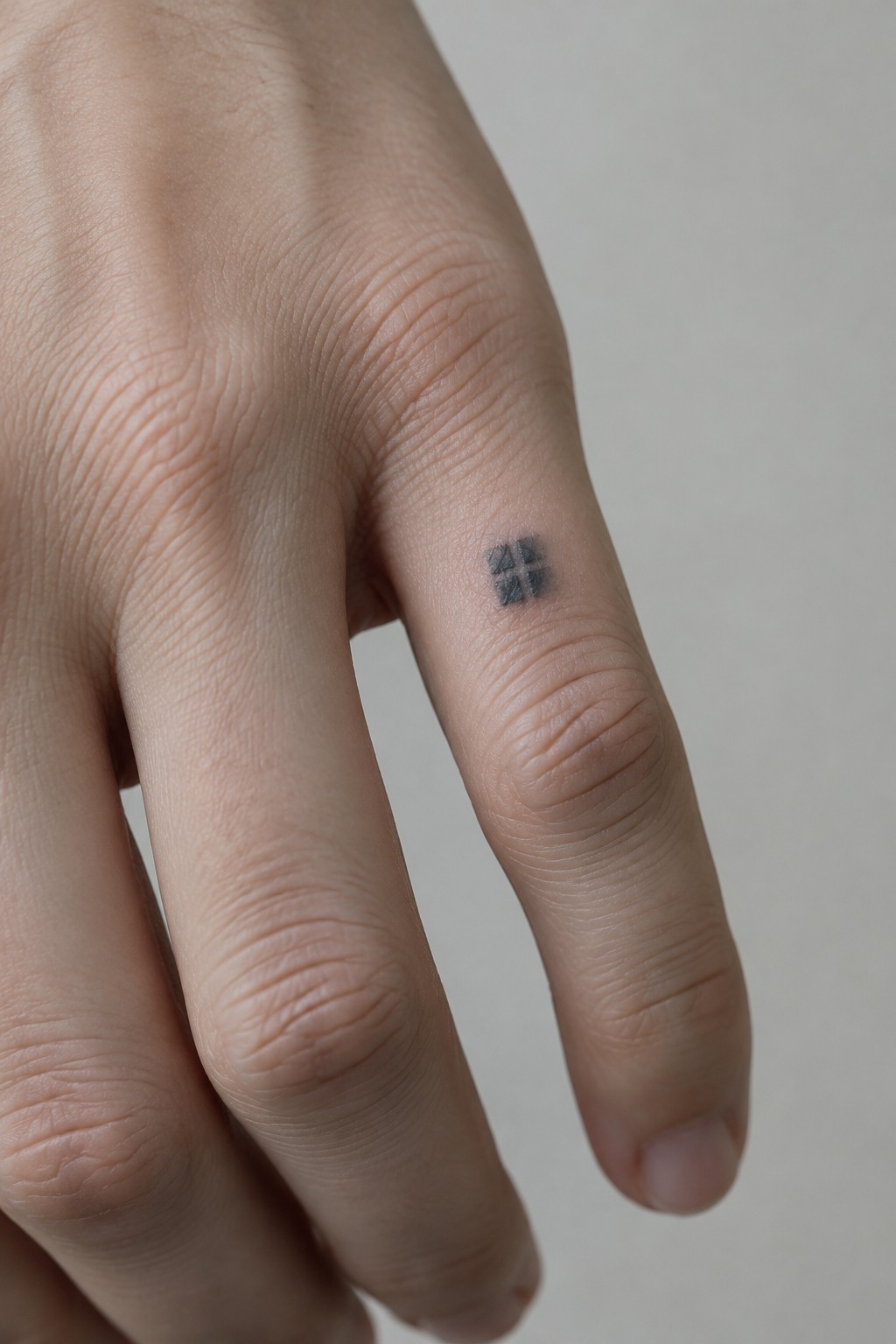 Hand with small black windowpane tattoo on ring finger skin.