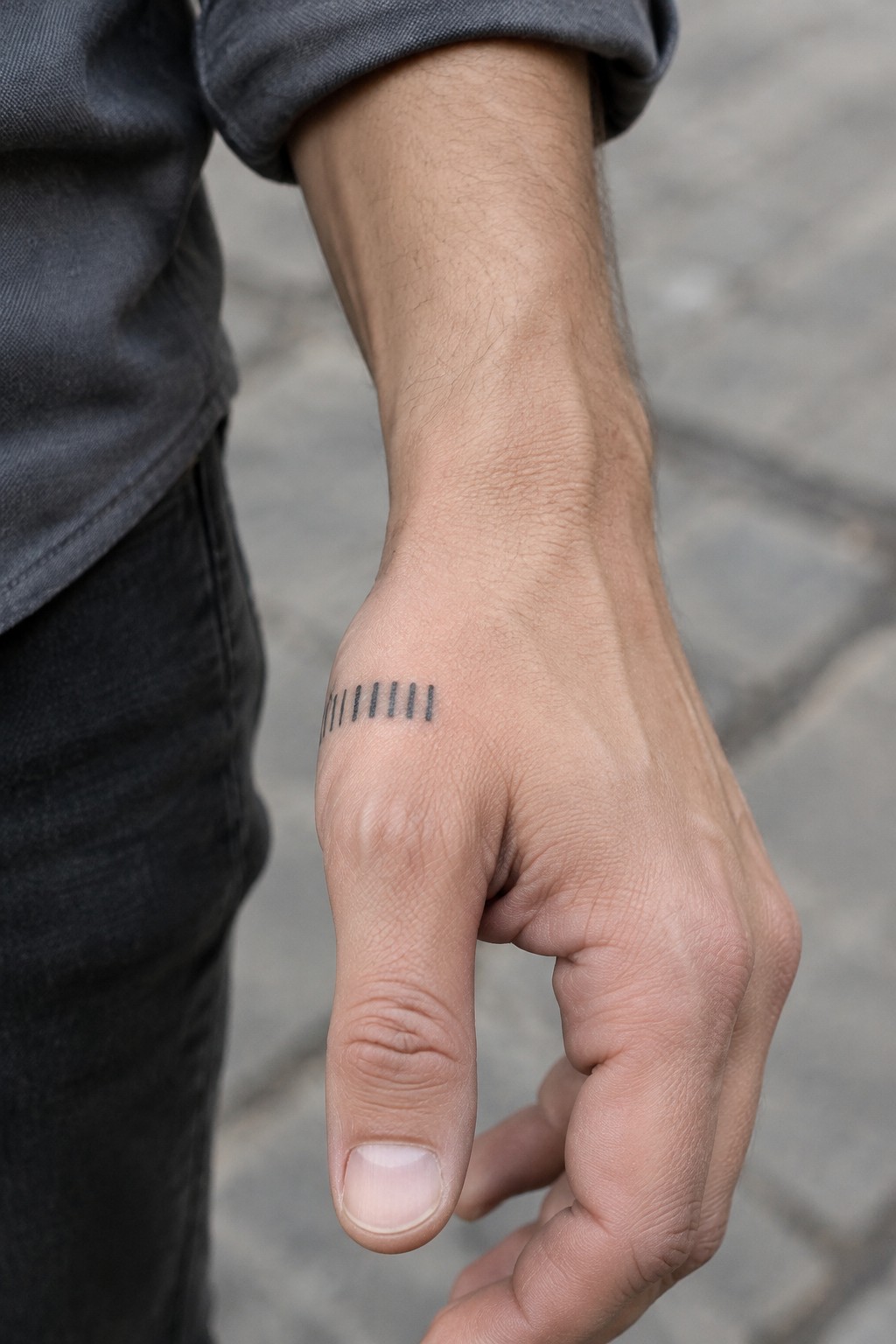Hand with five vertical black tattoo lines, gray rolled-up shirt sleeve.