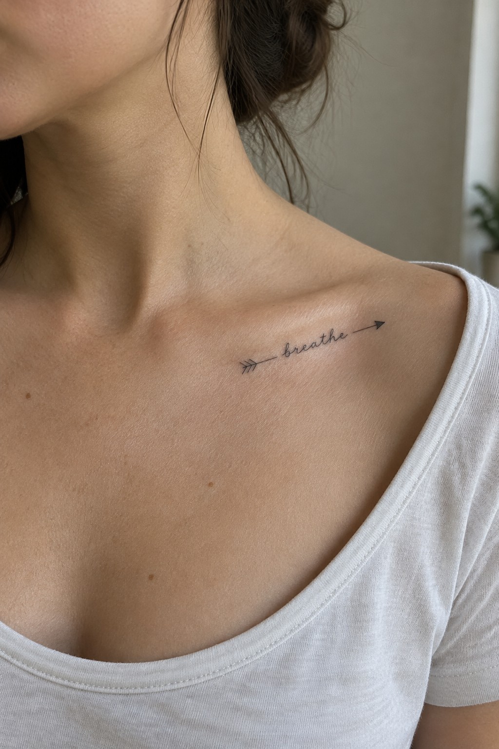 Fine line arrow tattoo with the word “breathe” across a woman’s collarbone.