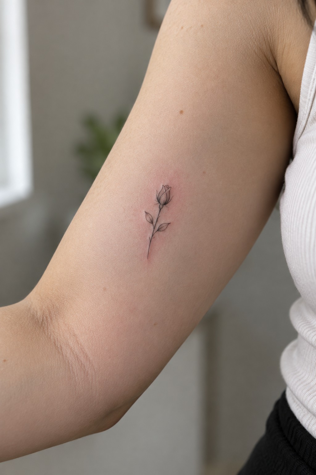Small fine line rose tattoo with a slender stem and two leaves on the inner arm.