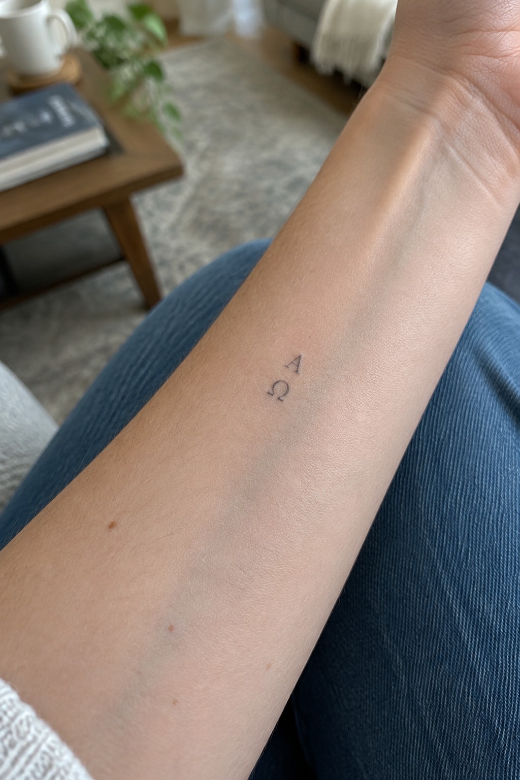 Light-skinned forearm with small A and Ω tattoo on blue corduroy pants
