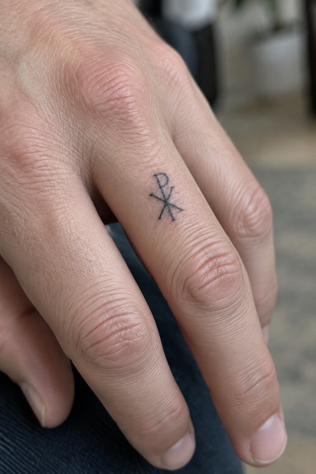 Small black chi rho symbol tattoo on the side of a finger in minimalist style.