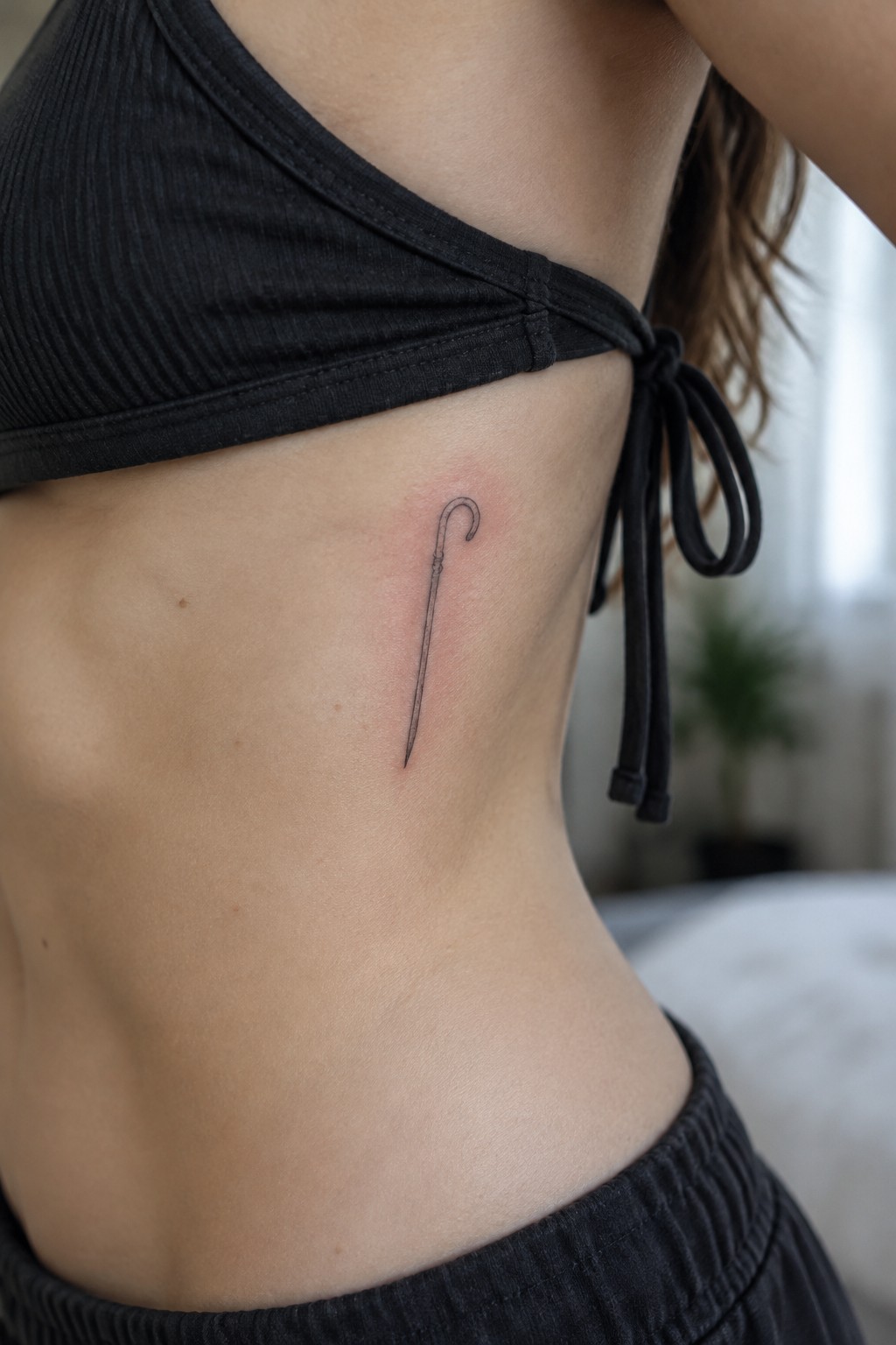 Woman's midriff with fresh umbrella tattoo under black ribbed crop top with ties