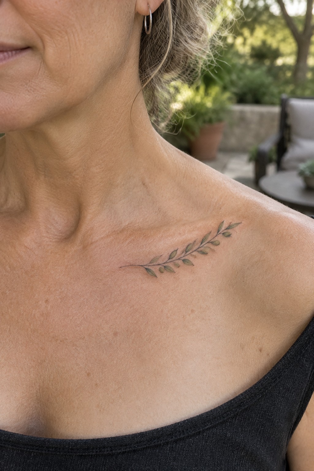 Woman's shoulder with delicate green leafy branch tattoo above black tank top