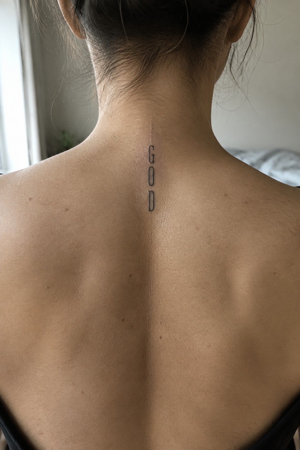 Vertical GOD tattoo centered on nape of neck above black top