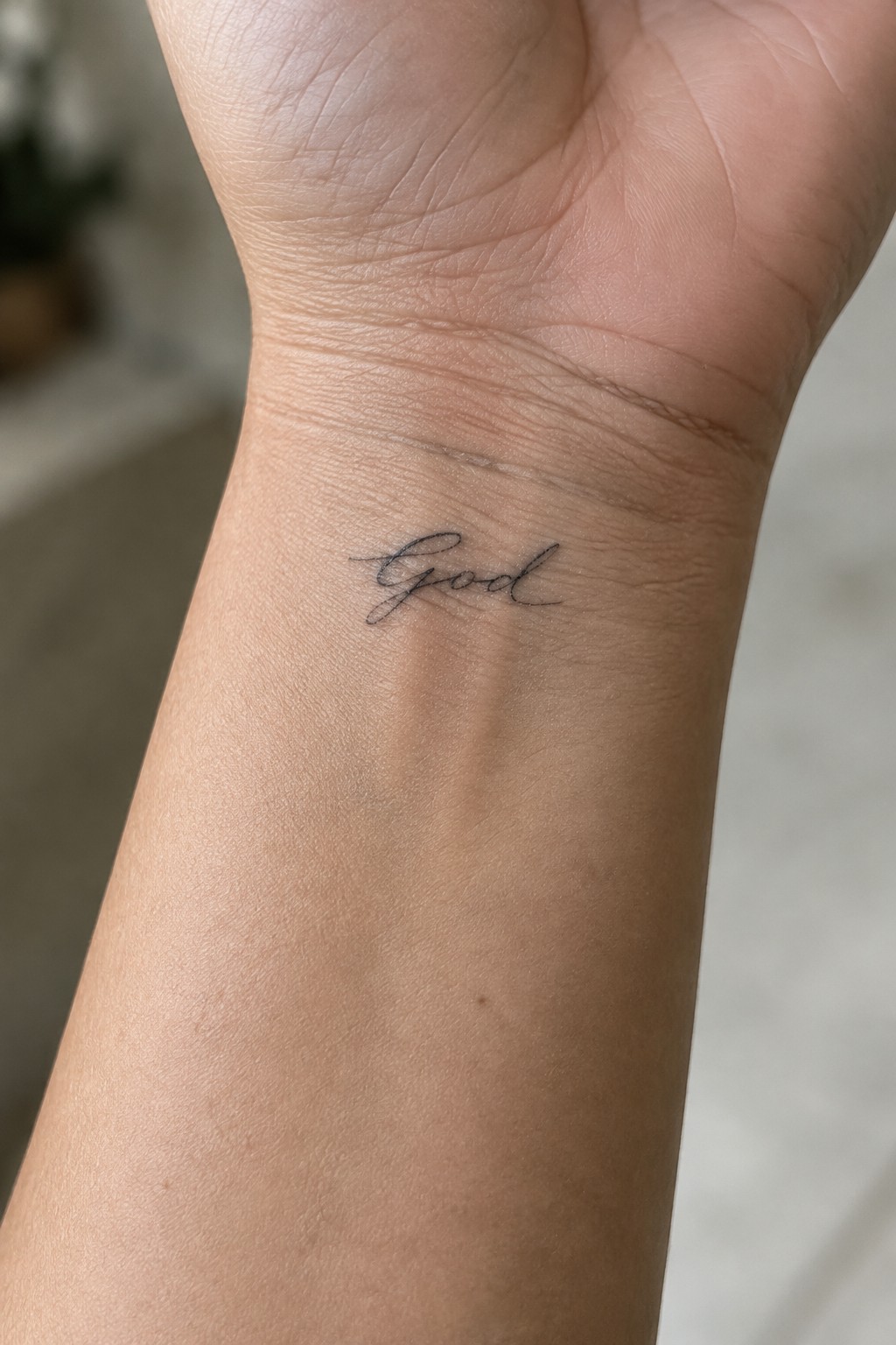 Inner wrist with delicate black cursive script tattoo reading