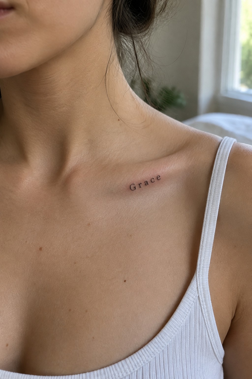 Woman's collarbone with black 'Grace' tattoo above white ribbed tank top strap