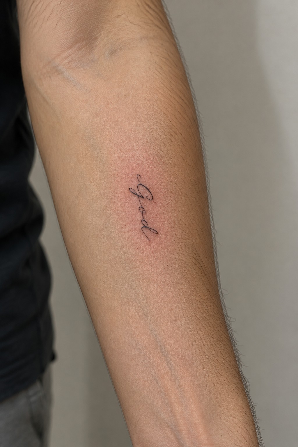 Small black cursive tattoo of the word god on the inner forearm