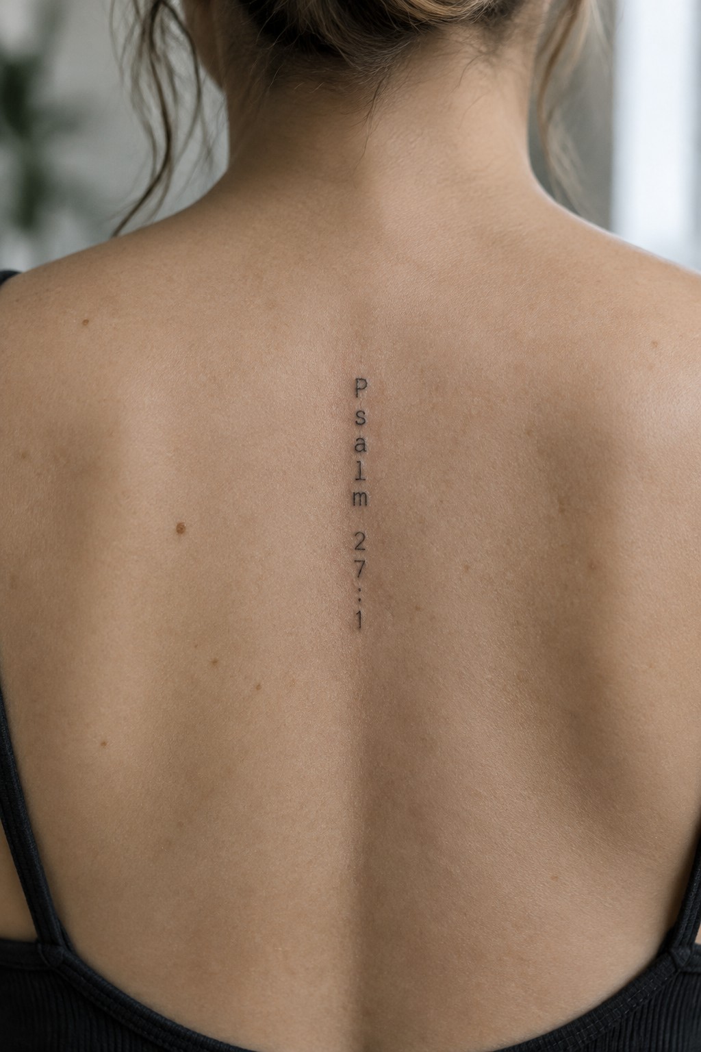 Woman's back with vertical Psalm 27:1 tattoo above black spaghetti straps