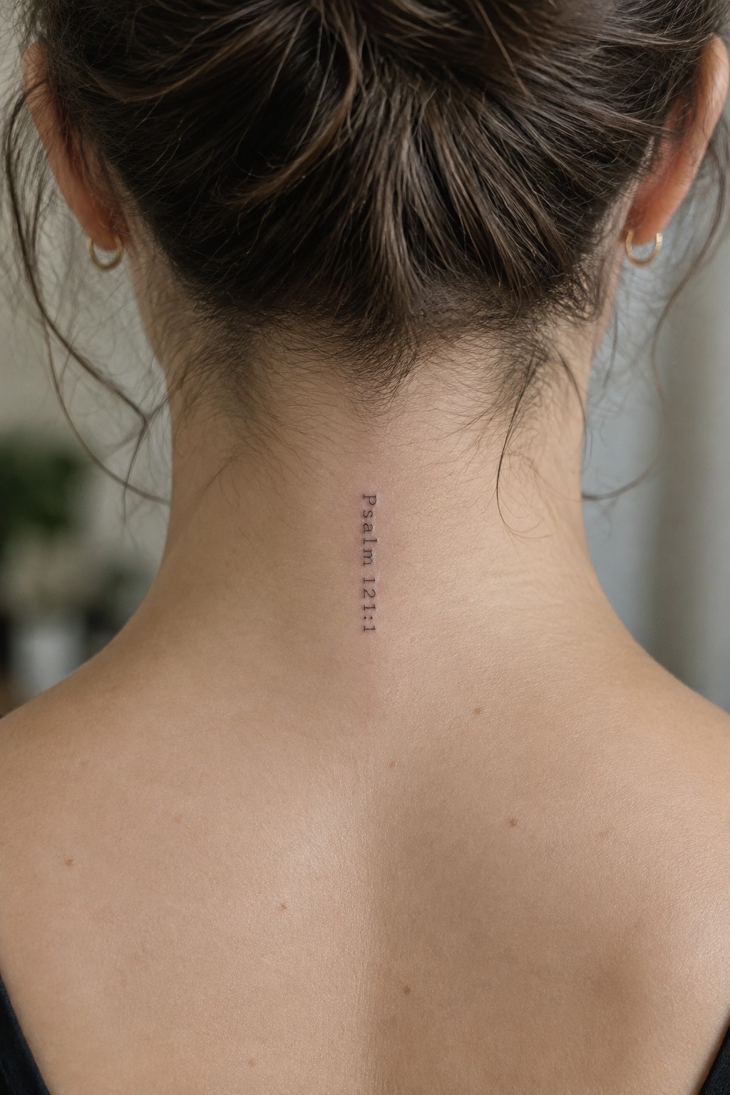 Woman's neck with vertical Psalm 121:1 tattoo, hair in bun, gold earrings