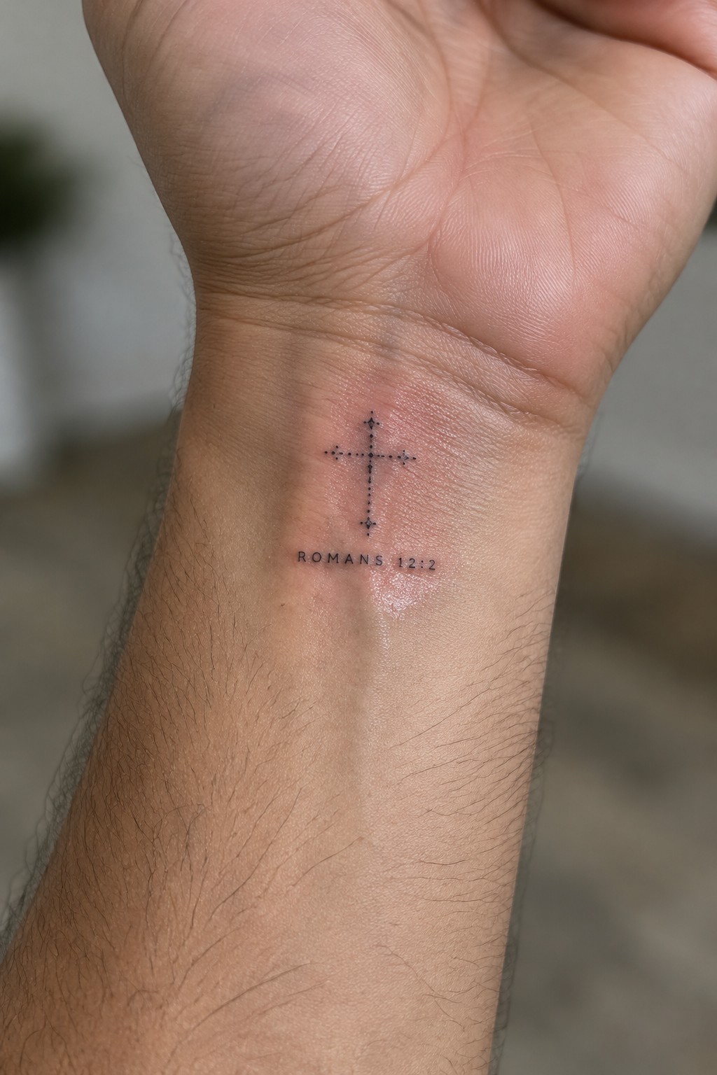 Dotted cross tattoo with Romans 12:2 text on inner wrist skin