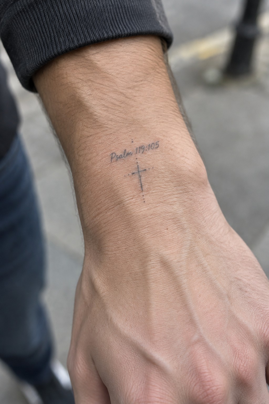 Minimalist cross tattoo on the inner wrist with Psalm 119:105 text above it in fine lines and dots