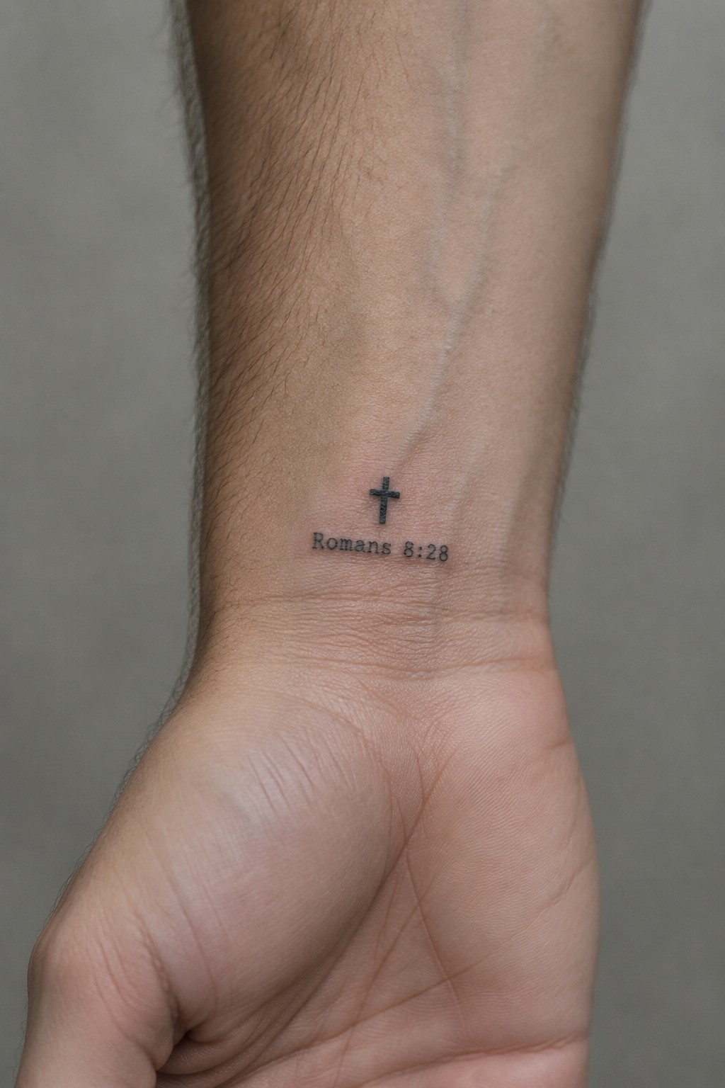 Small cross and Romans 8:28 tattoo on inner wrist of clenched fist