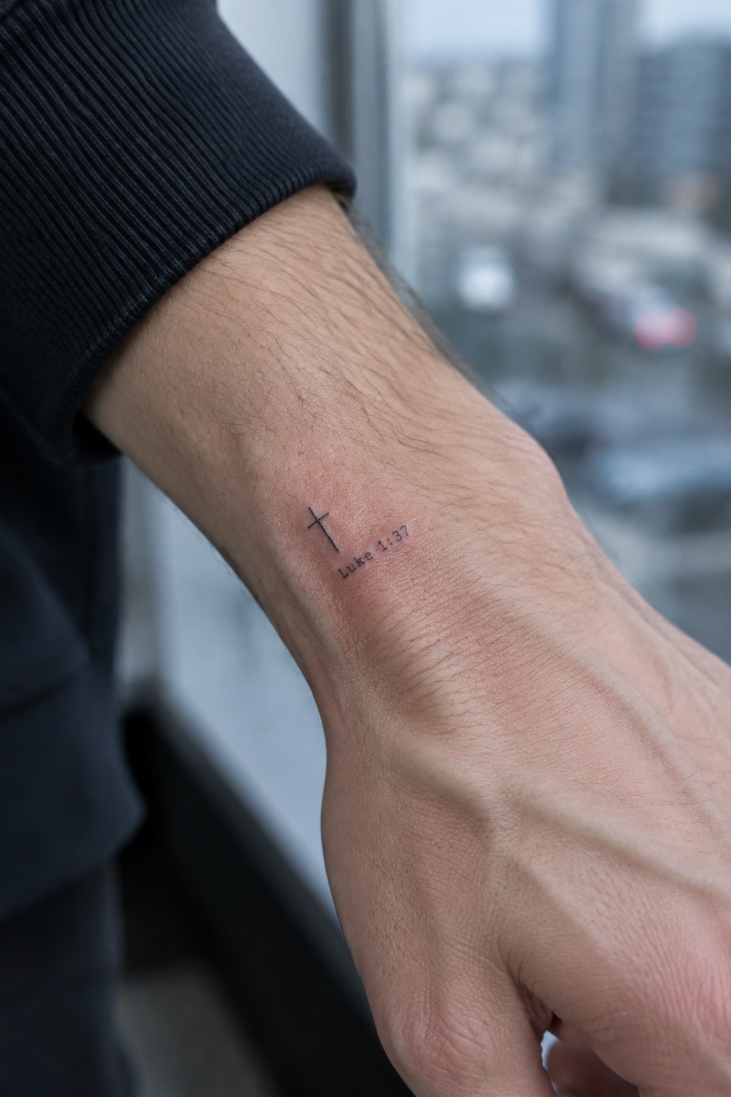Wrist with black cross tattoo and Luke 1:37 text, dark ribbed sleeve, blurred window view