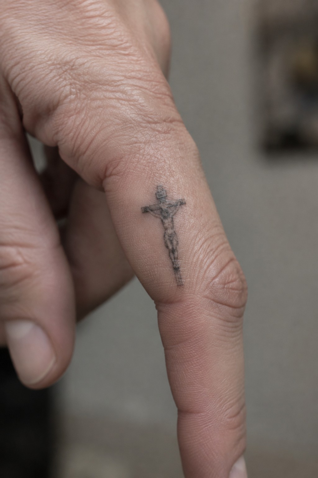 Small black ink crucifix tattoo with Jesus figure placed along the side of a finger
