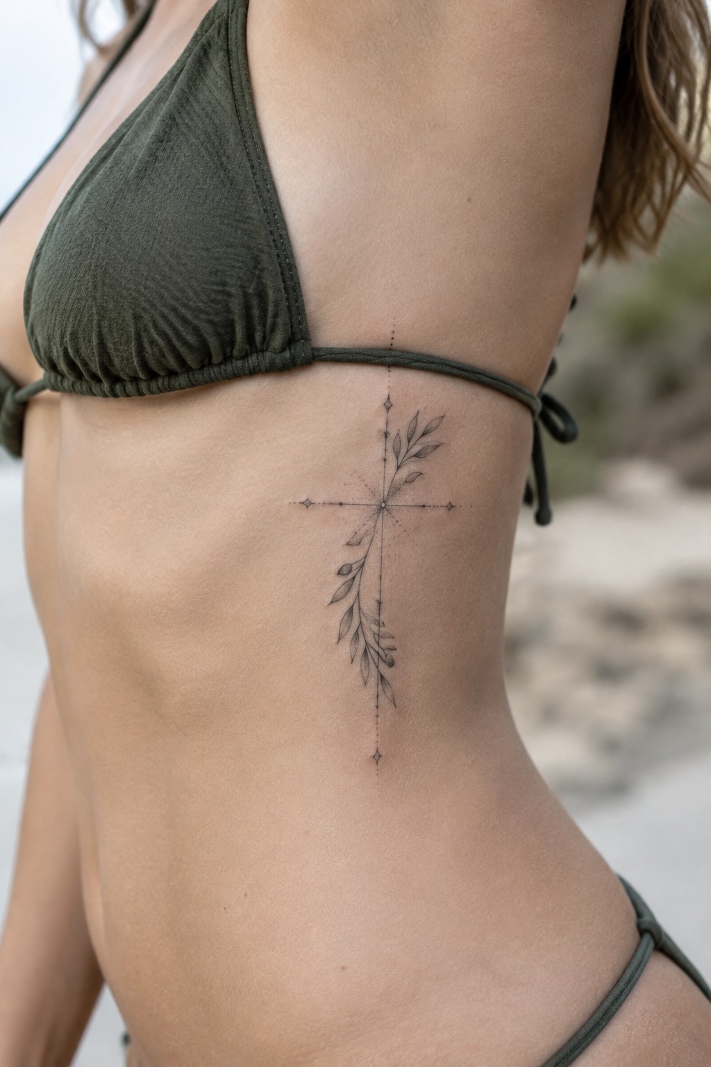 Woman's midriff in olive green bikini with black cross-and-leaves tattoo on side