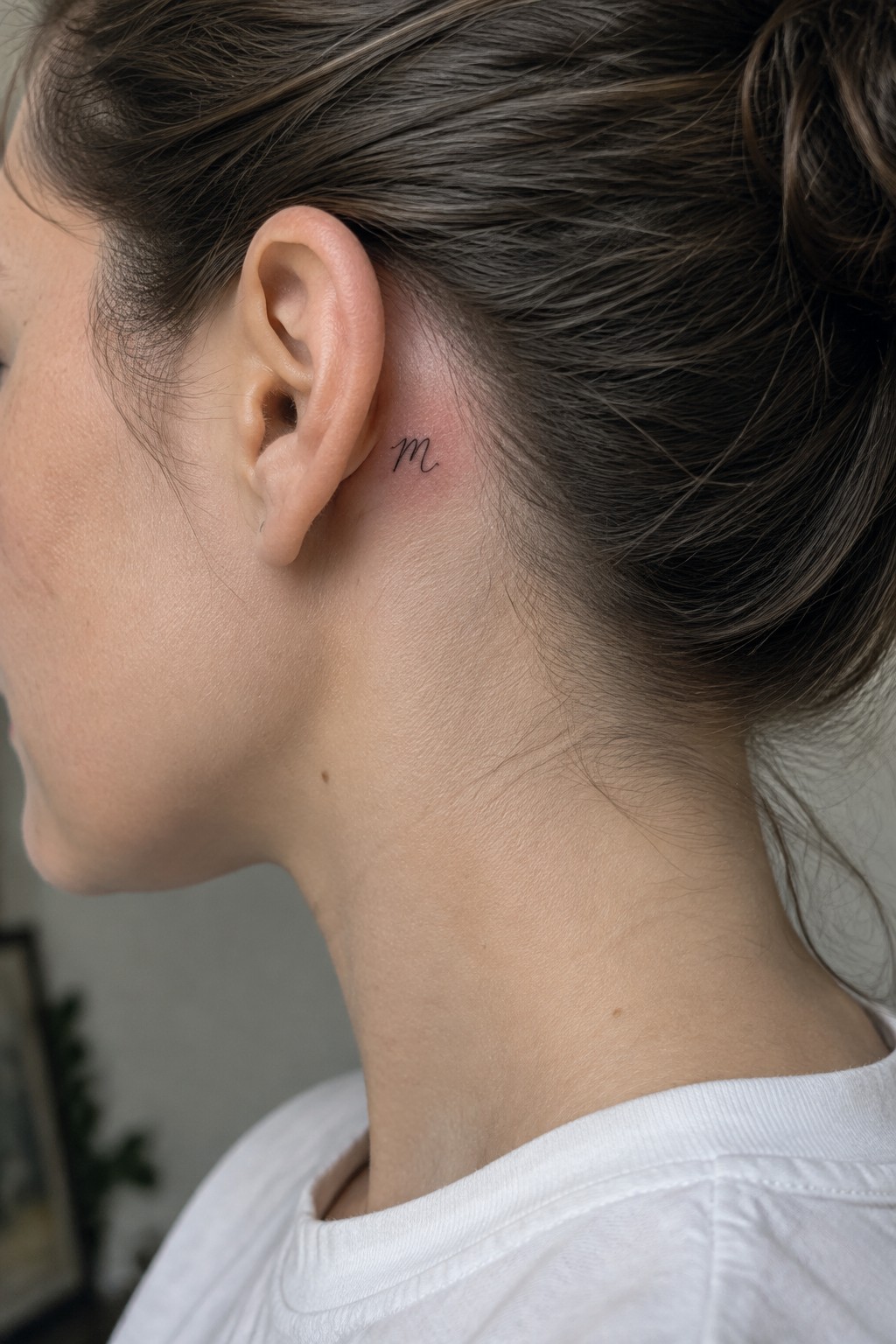 Small black Scorpio zodiac glyph tattoo behind a woman’s ear.