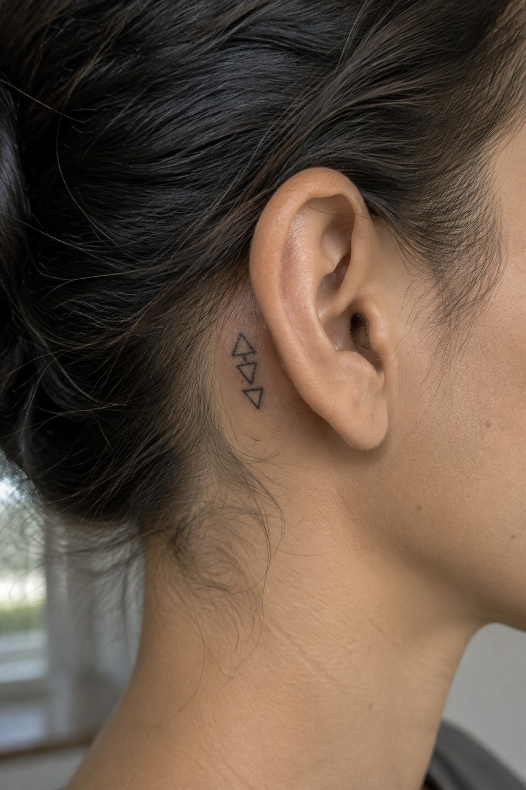 Three small outlined geometric triangles in alternating directions tattooed behind a woman’s ear.
