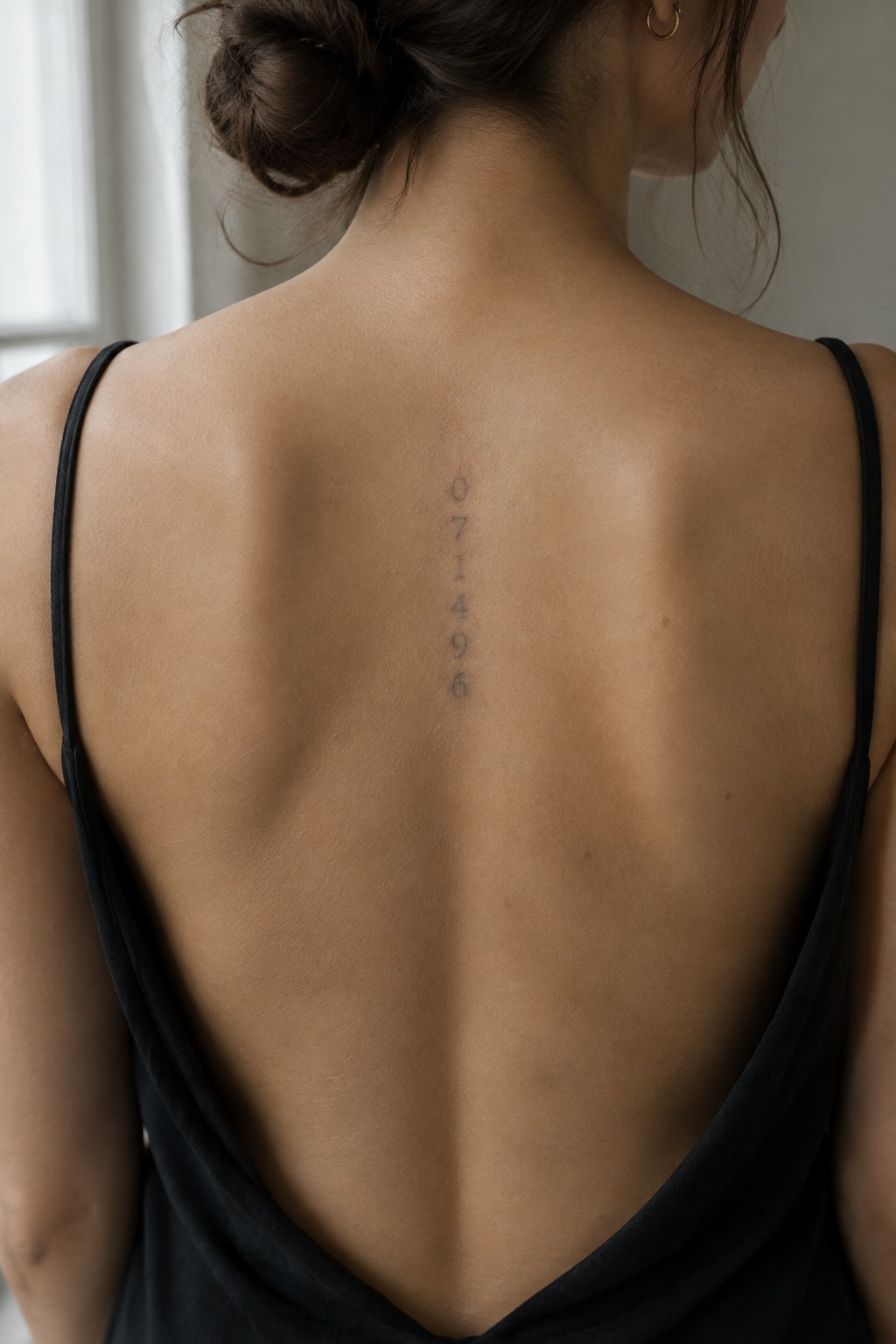 Fine-line numerals arranged vertically along a woman’s upper spine.