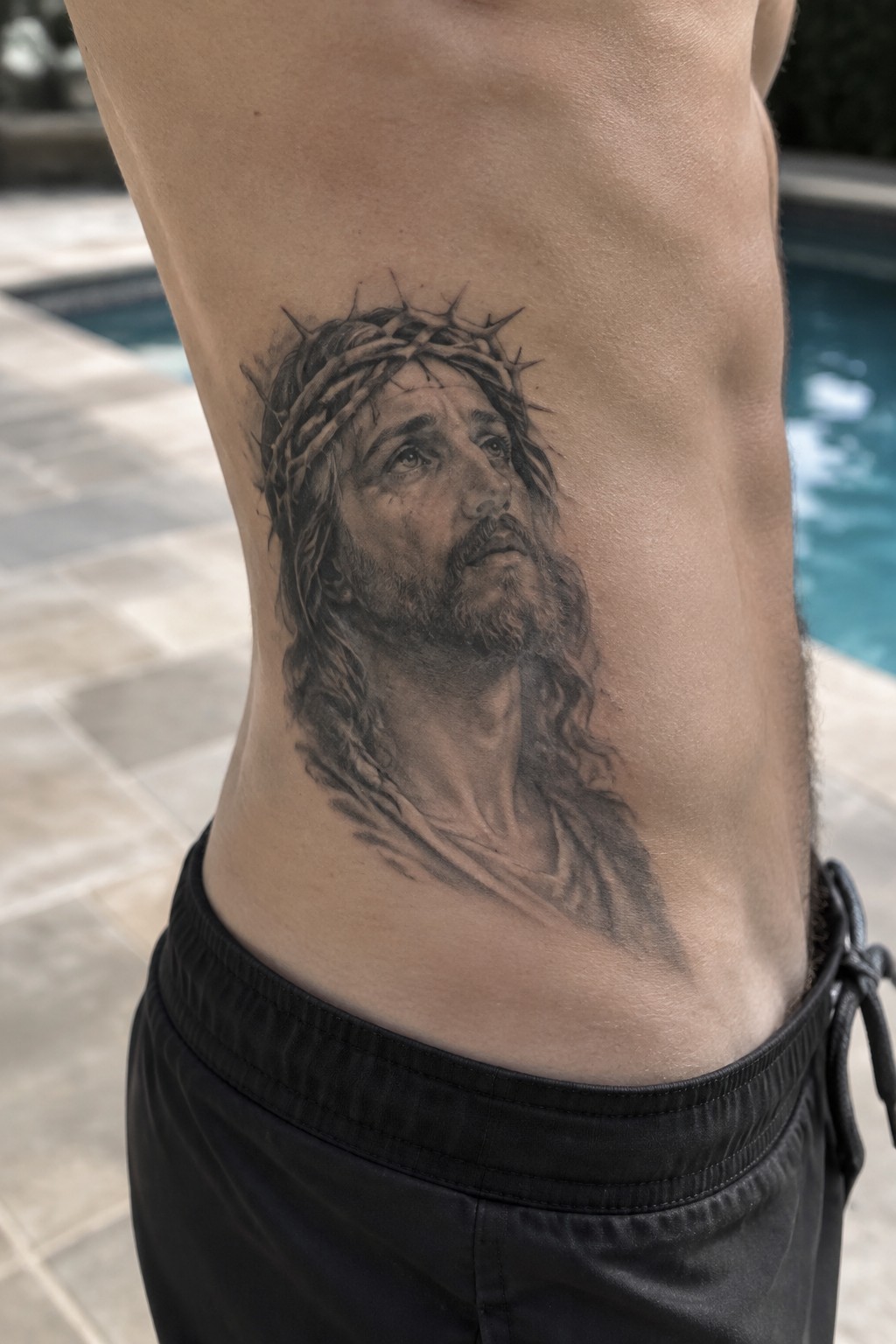 Black and gray Jesus tattoo with crown of thorns on side by pool