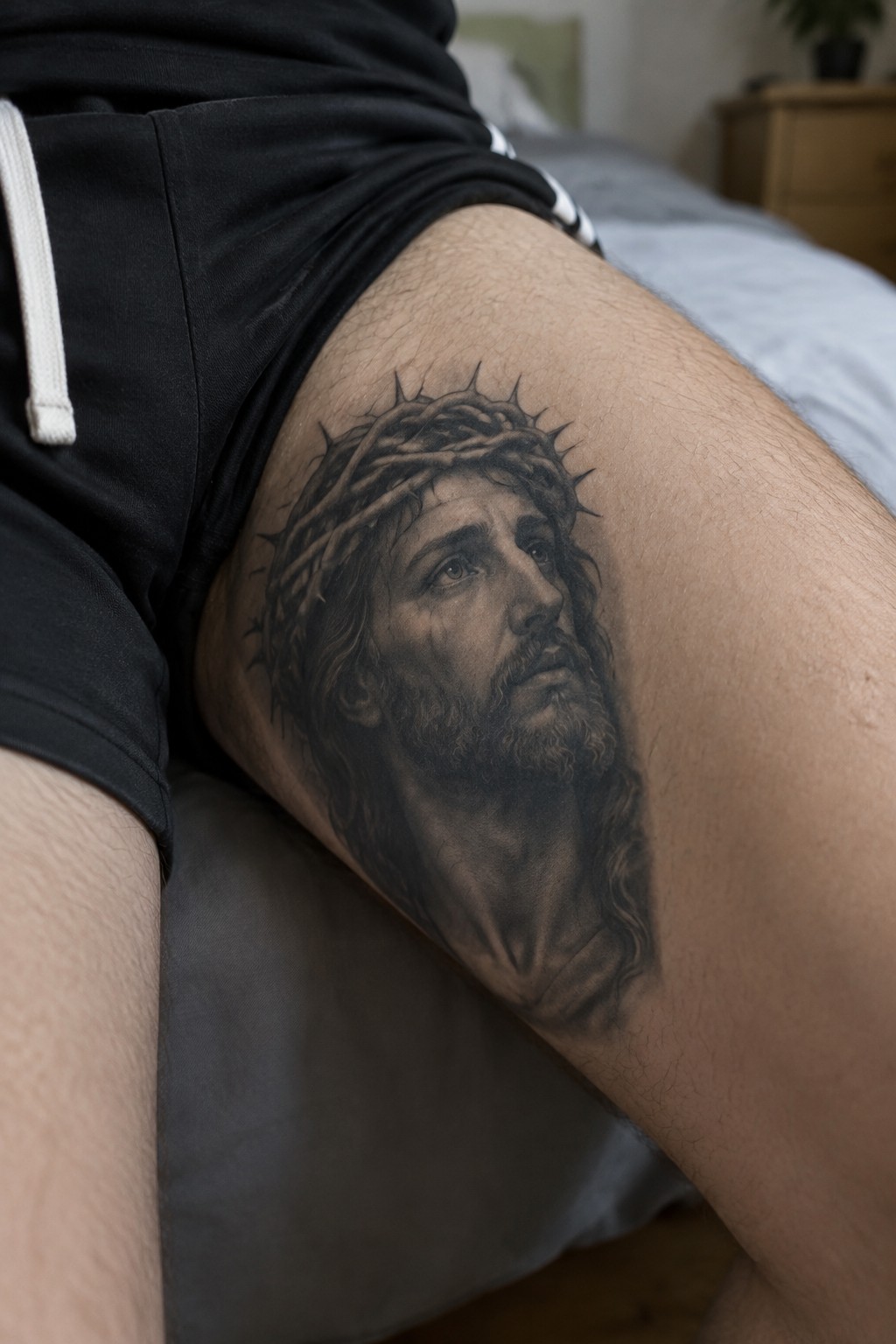 Large realistic black and grey tattoo of Jesus with crown of thorns on the upper thigh.