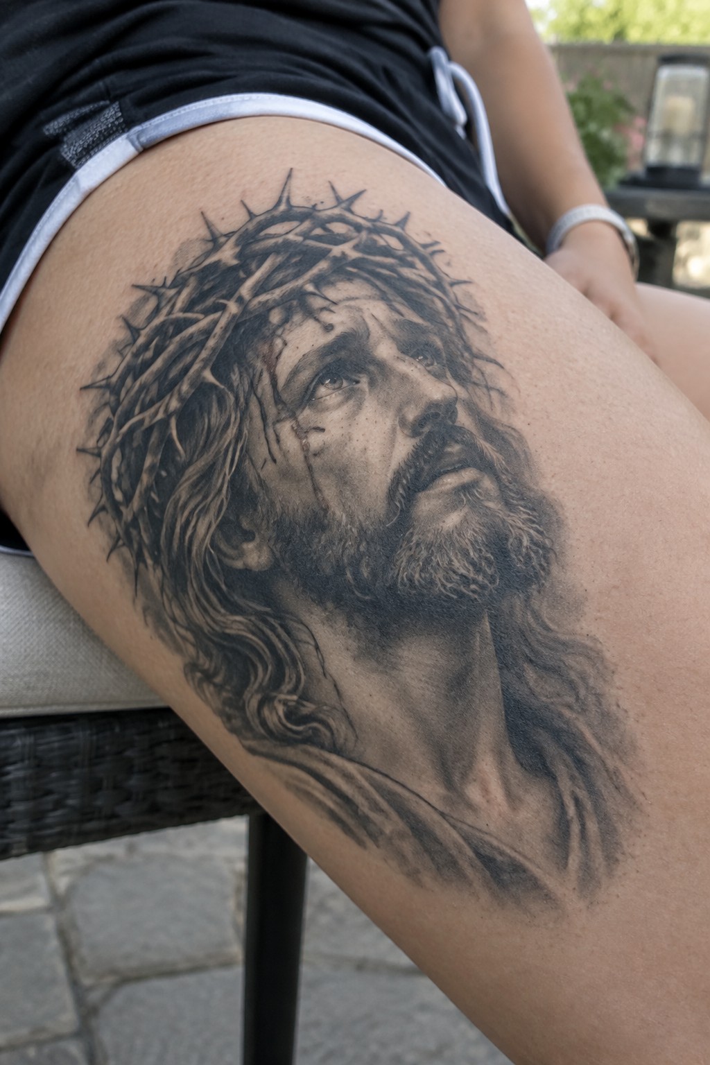 Large realistic black and grey tattoo of Jesus with crown of thorns on the thigh