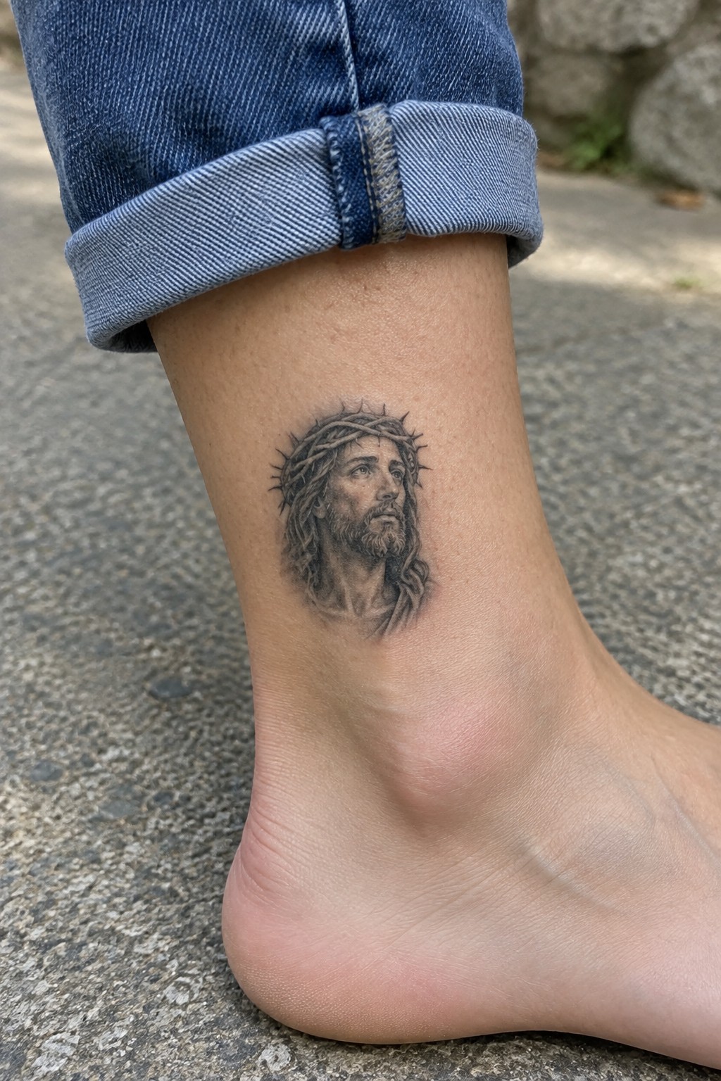 Realistic black and grey Jesus Christ portrait tattoo with crown of thorns on the ankle above the foot.