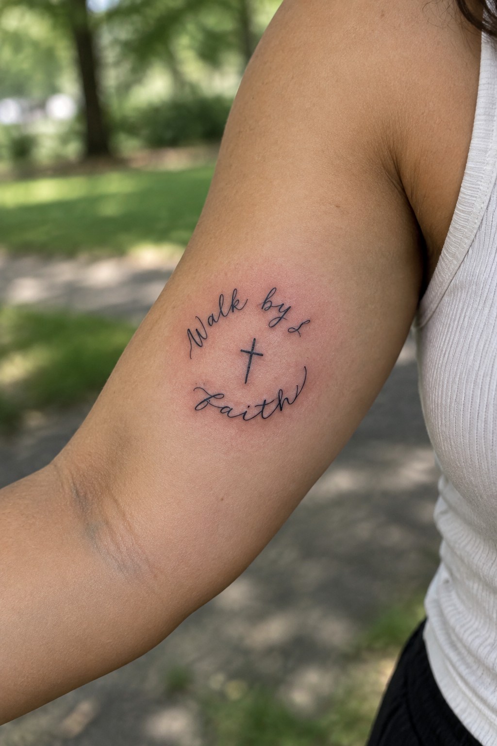 Fine-line “Walk by faith” script tattoo with a small cross on the inner arm.