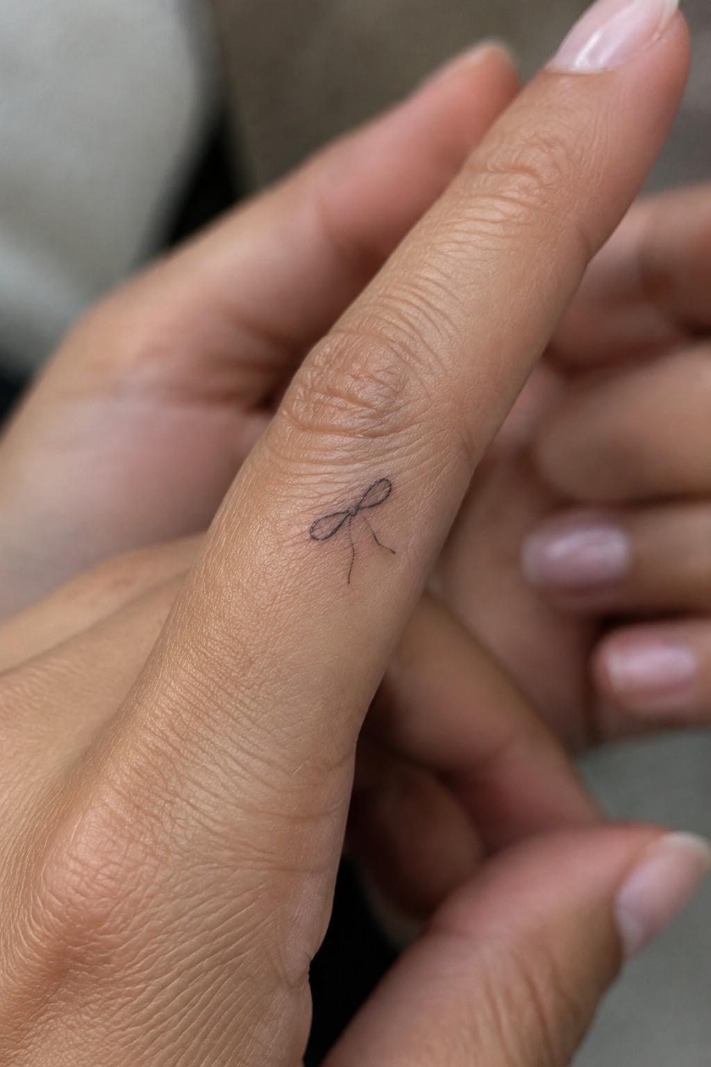Small black bow tattoo on side of manicured index finger with pink nail