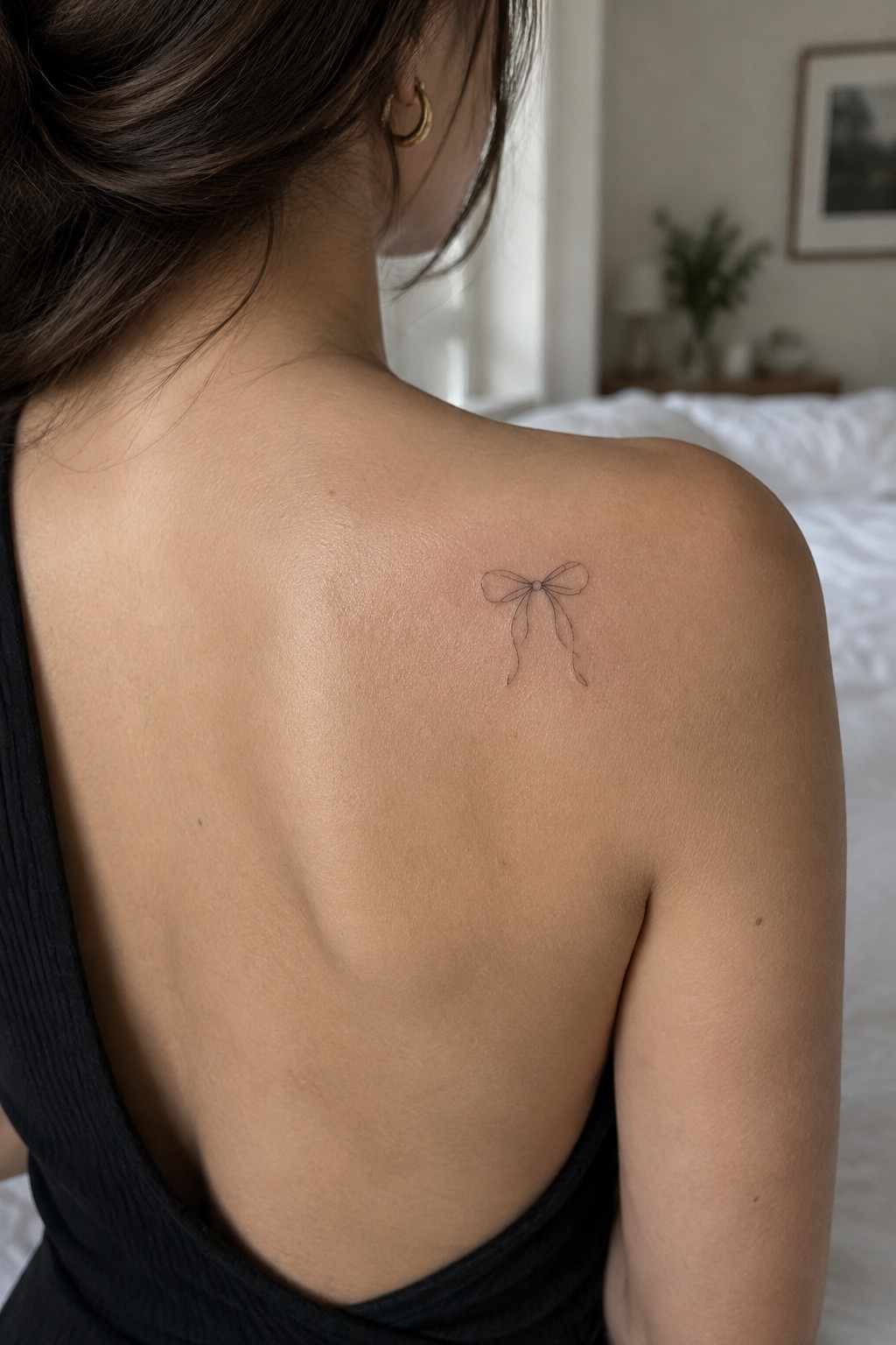 Woman's upper back with small bow tattoo on shoulder, black sleeveless top